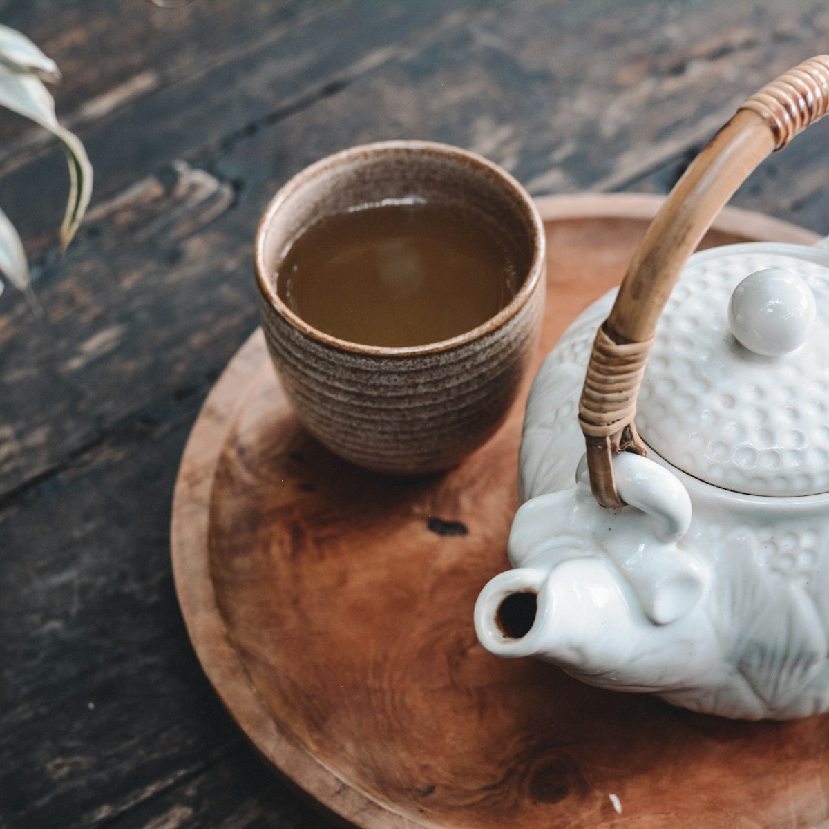 Ceramic cup of green tea and a teapot on a wooden tray