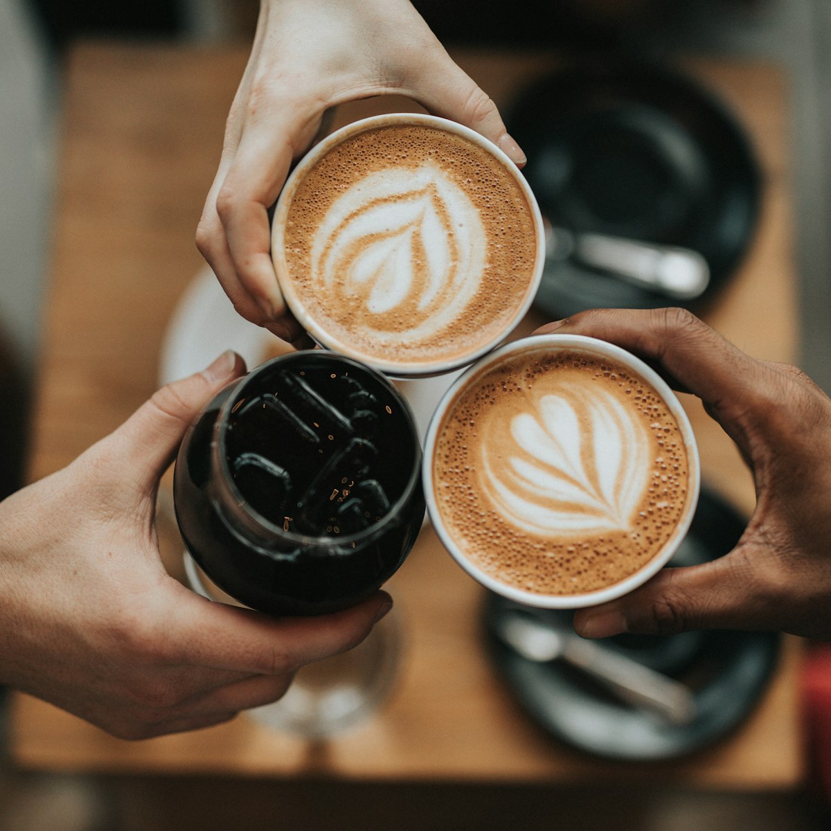 Three hands raising flat whites with latte art over a café table